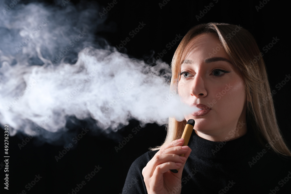 Obraz premium Young woman using electronic cigarette on black background