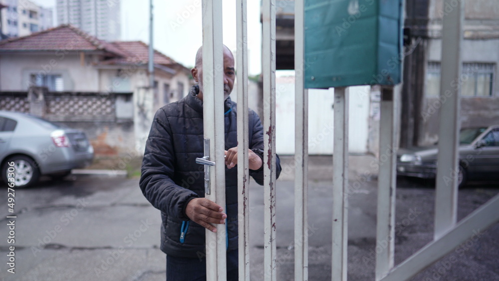 An older man leaving house in the drizzle opening entrance door and going out to street An older man leaving house in the drizzle opening entrance door and going out to street