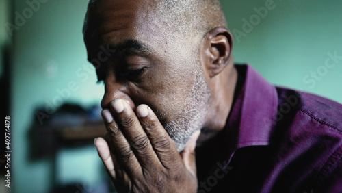 A worried senior black man praying to God seeking help