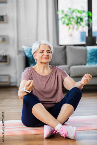 sport, fitness and healthy lifestyle concept - happy senior woman meditating on exercise mat at home