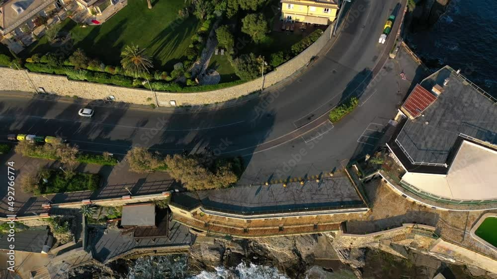 Aerial view of traffic on a coastal road, revealing the cityscape of east Genova,, Italy - reverse, tilt, drone shot