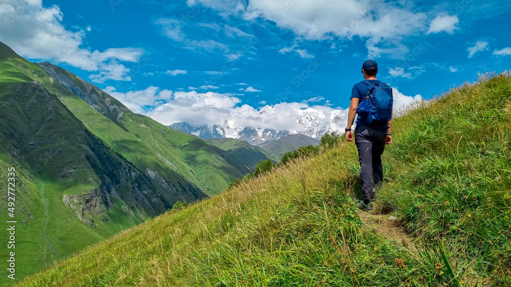 A male backpacker on a hiking trail to Chubedishi viewpoint. There is an amazing view on the Shkhara Glacier,near the village Ushguli the Greater Caucasus Mountain Range in Georgia, Svaneti Region