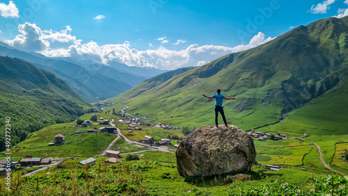 A man standing on a rock with an aerial view on the village Ushguli, near the Shkhara Glacier in the Greater Caucasus Mountains in Georgia, Svaneti Region.Chubedishi viewpoint.Patara Enguri River.Free photo