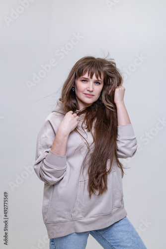 portrait of a pretty blonde girl with long hair in a beige hoodie on a light background