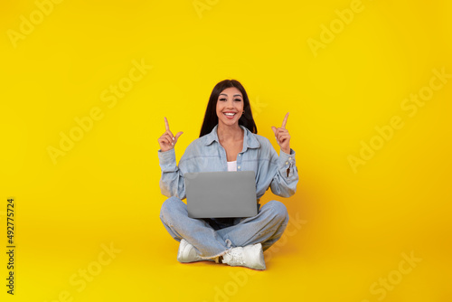 Happy lady using laptop pointing up at studio