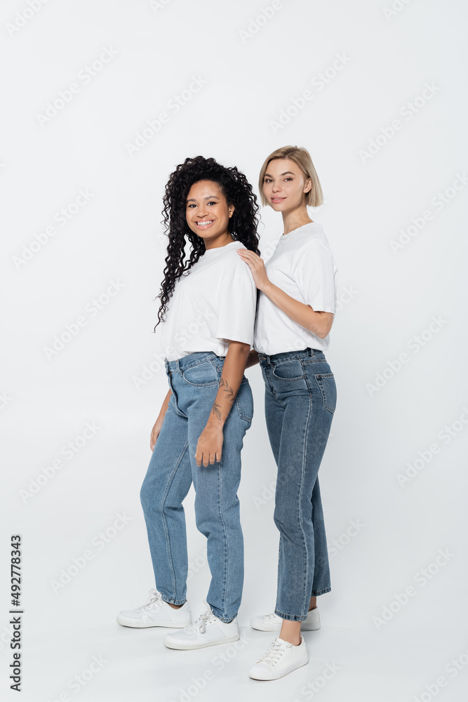 Full length of smiling woman hugging african american friend on grey background. Full length of smiling woman hugging african american friend on grey background.