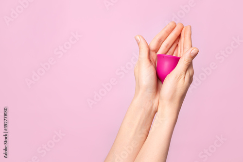Mature content A young woman holds a pink menstrual cup in her hand. Pink colored background. Space for text. Eco-friendly silicone women s health cycle