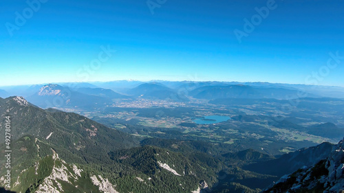 A panoramic view on the Alps from the top of Mittagskogel in Austrian Alps. Clear and sunny day. There is a lake at the bottom. A bit of haze in the valley. Outdoor activity. Alpine mountain chains © Chris