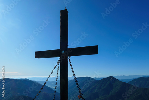 A wooden cross on top of Hohe Weichsel, Alpine peak in Austria. The cross is supported by 4 metal ropes. There are endless mountain chains behind it. Early fall. The slopes are turning golden photo