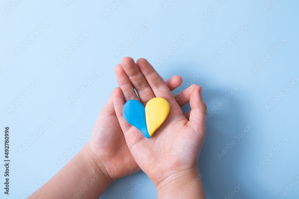 Heart of yellow-blue colors of the national flag of Ukraine in a childs hands, top view. Love for the motherland in the children's heart concept Heart of yellow-blue colors of the national flag of Ukraine in a childs hands, top view. Love for the motherland in the children's heart concept