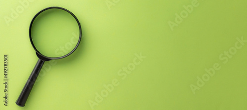 Photo of magnifier glass on left side over green pastel background with copyspace for put your text or logo.,Flat lay top view mock-up item concept.