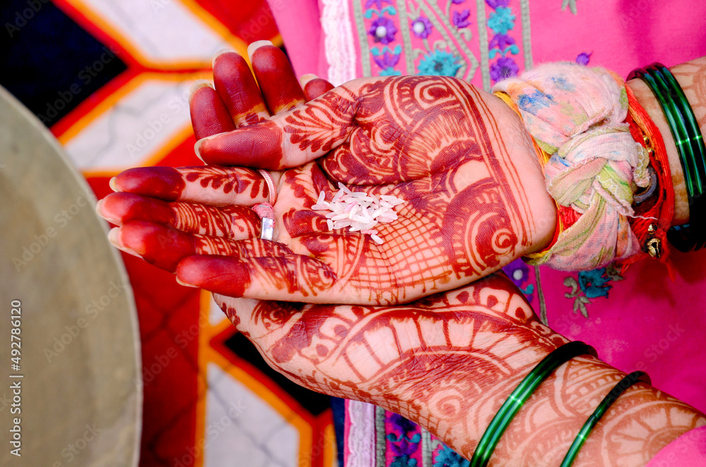 Indian bride performing rites holding some rice in his mehndi designed hands during wedding ceremony.