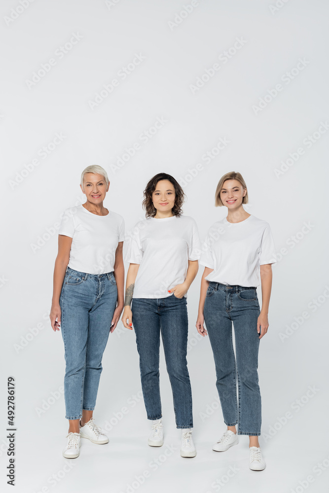 Full length of smiling women in white t-shirts standing on grey background. Full length of smiling women in white t-shirts standing on grey background.