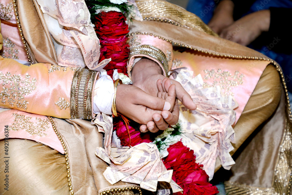 Indian groom performing rites holding some rice in his mehndi designed hands during wedding ceremony.