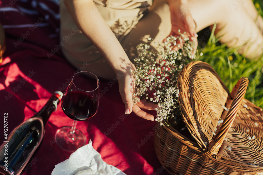 Woman in dress sits alone on an outdoor picnic and touches the flowers from basket. Picnic in the park. 