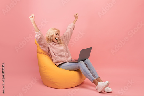 Tableau sur toile Excited lady making YES gesture, sitting in beanbag chair with laptop and celebr