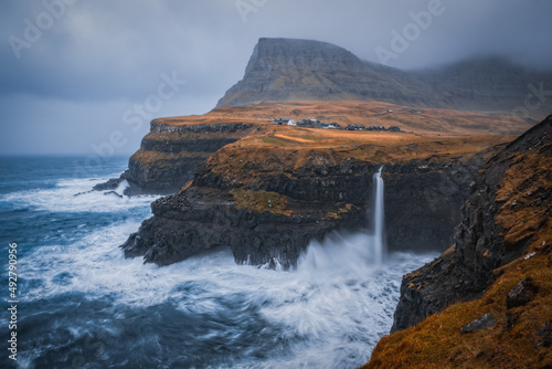 Dramatic view of Mulafossur waterfall with Gasadalur village on background. Vagar island  Faroe Islands  Denmark. November 2021.