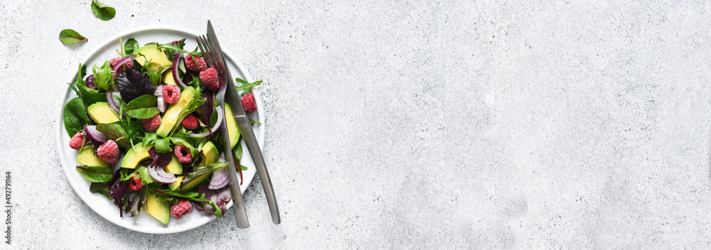 Mix salad with arugula, avocado and raspberries on a stone concrete background. View from above