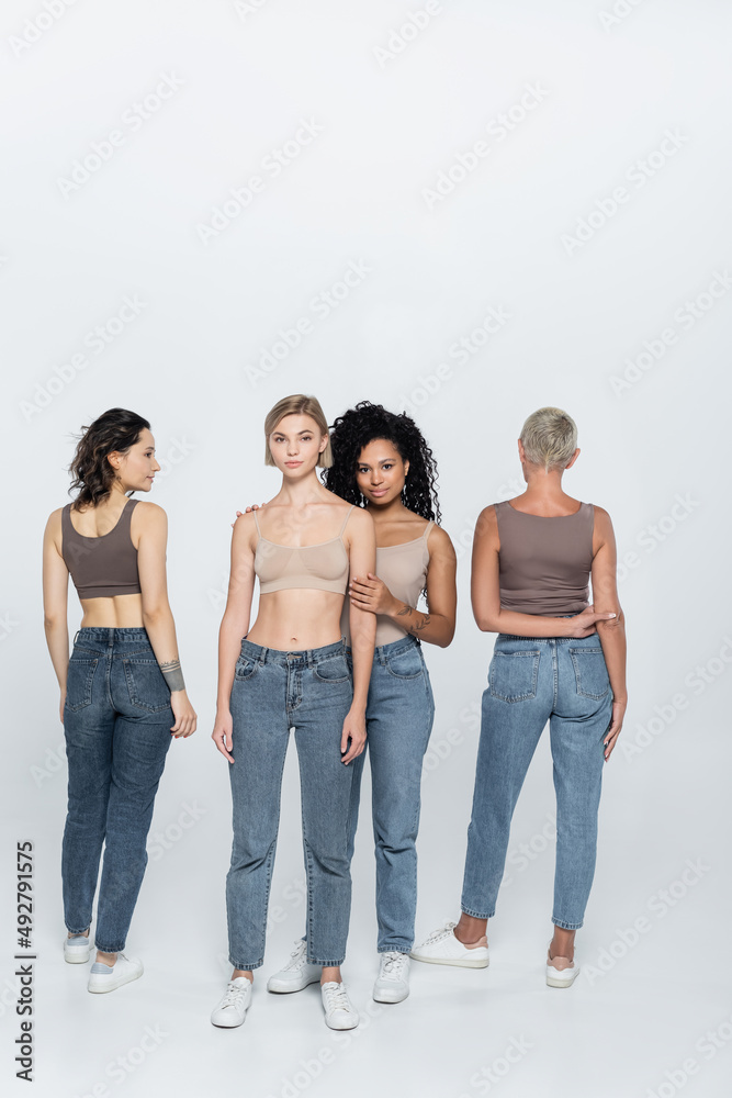 Full length of african american woman hugging blonde friend on grey background. Full length of african american woman hugging blonde friend on grey background.