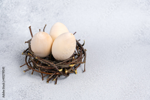 Wooden eggs for creativity and coloring. Three eggs in bird's nest made of branches on light gray textured background with copy space. Preparation for Easter, homemade decor.