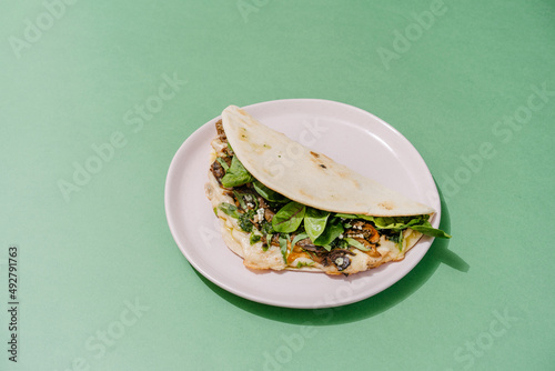 Italian Piadina with oyster mushrooms, spinach, pesto, mozzarella, bechamel, gorgonzola cheese, green onions. Green background. Copy space photo