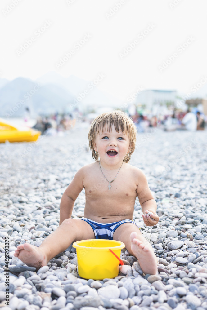 Cute child playing with yellow bucket and toy car on pebble beach. Happy toddler on sea coast. Summer family holiday vacation. Two years old little boy having fun. Summertime. Travel concept Cute child playing with yellow bucket and toy car on pebble beach. Happy toddler on sea coast. Summer family holiday vacation. Two years old little boy having fun. Summertime. Travel concept