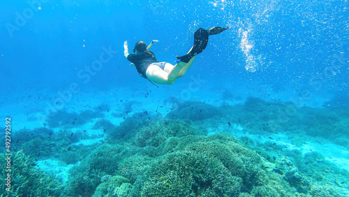 A woman in masker and fins snorkelling in a vivid coral reef in Komodo National Park, Indonesia. She is diving to see the reef from closer. Crystal clear water. Air bubbles around him. Free diving