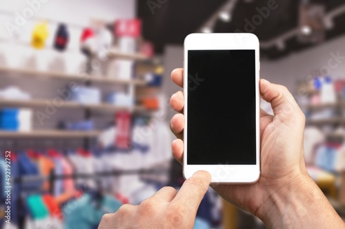 Blank screen in a smartphone in a human's hand in a clothing store in a shopping mall.