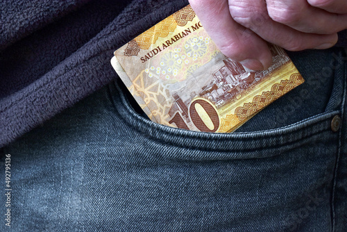 Man hand putting 10 Saudi riyal banknotes in the front pocket of jeans. photo