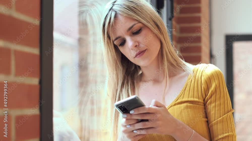 Video of young woman using her mobile phone while standing next to the window at home. Video of young woman using her mobile phone while standing next to the window at home.