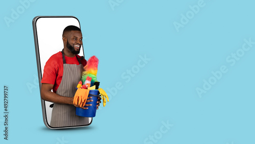 Black Male Cleaner With Basket With Detergents Peeking Out Of Smartphone Screen