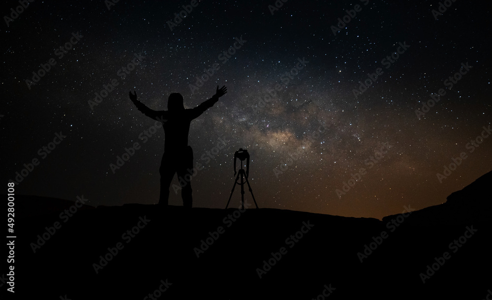 Silhouette of a standing Photographer  with Dark Space background on the mountain.Milky Way. Night sky with stars,with noise and grain. 