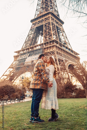 A couple kissing in front of the Eiffel Tower in Paris. Romantic trip, honeymoon in Europe. France city of love © MoreThanProd