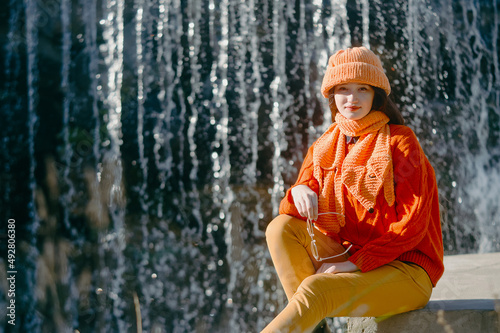 autumn portrait of a girl in a hat and orange sweater. woman sitting on the river bank.