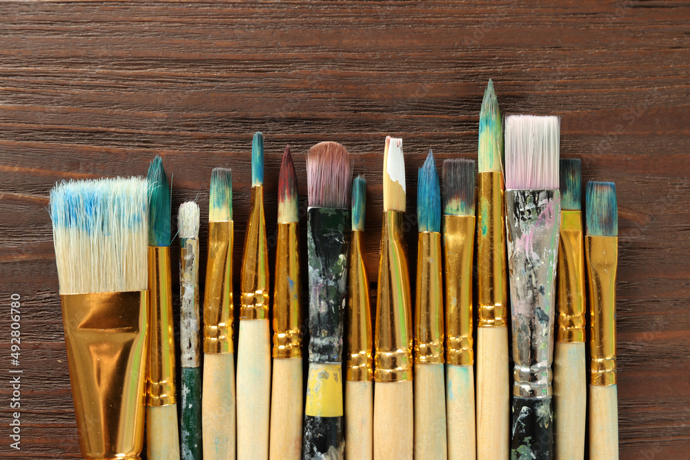 Fototapeta premium Many paintbrushes on wooden table, flat lay