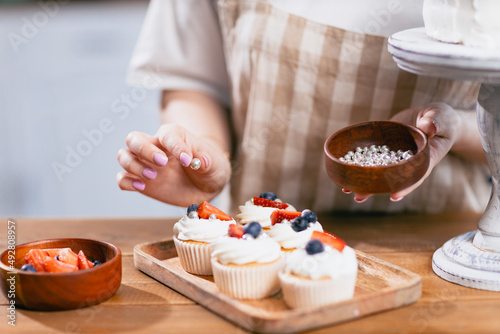 Pastry chef confectioner hand put decorate cake with berry on kitchen table.