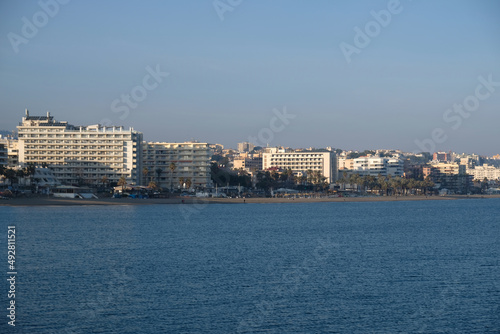 View of high-rise resort hotels or residential buildings on Mediterranean coast in Malaga, Andalusia, Spain. View of sandy beach, palm trees, blue sea, blue sky and mountains. Real estate concept. © Yuliya