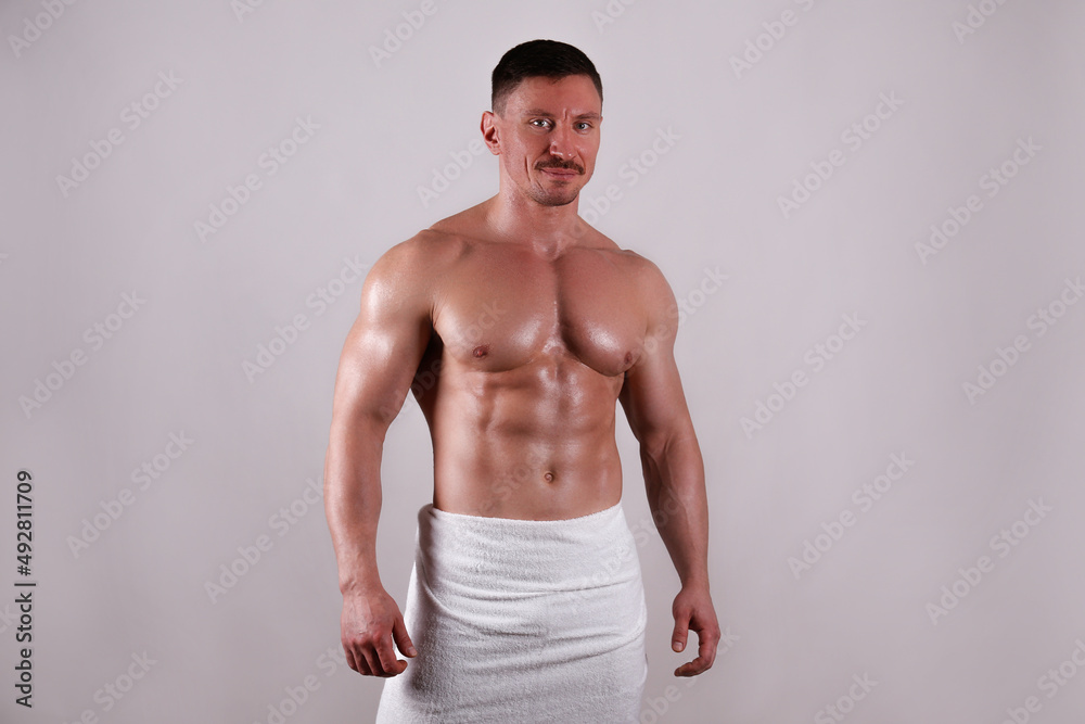 Fototapeta premium Professional bodybuilder wearing just a towel posing over isolated grey background. Studio shot of a shirtless fit guy flexing the muscles. Close up, copy space.