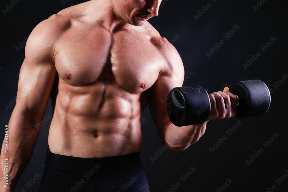Professional bodybuilder performing exercise with dumbbells over isolated black background. Studio shot of a male fitness model pumping iron. Close up, copy space.