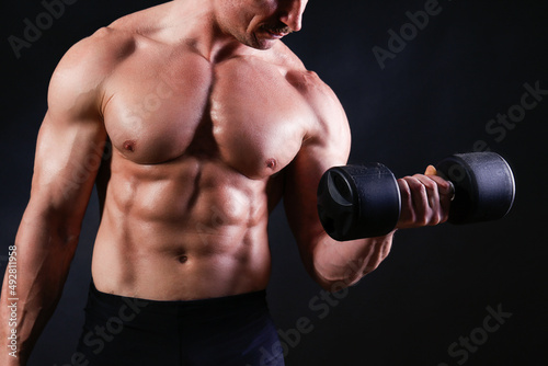 Professional bodybuilder performing exercise with dumbbells over isolated black background. Studio shot of a male fitness model pumping iron. Close up, copy space.