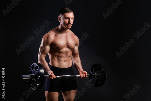 Professional bodybuilder performing biceps curls exercise with curved barbell over isolated black background. Studio shot of a fitness model with ez bar. Close up  copy space.