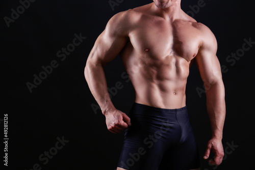 Professional bodybuilder posing over isolated black background. Studio shot of a fitness trainer flexing the muscles. Close up, copy space. © Evrymmnt