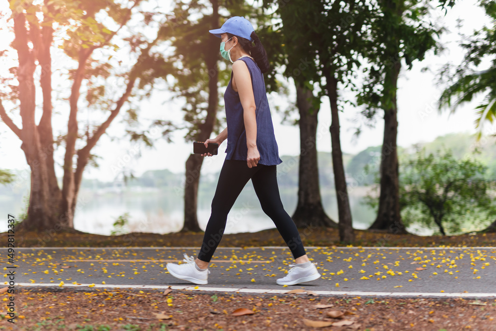 Full length of woman in medical mask exercise walking in the park. Full length of woman in medical mask exercise walking in the park.