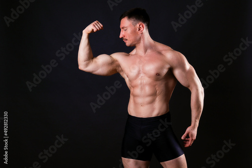 Professional bodybuilder posing over isolated black background. Front single Biceps pose. Studio shot of a fitness trainer flexing the muscles. Close up, copy space.