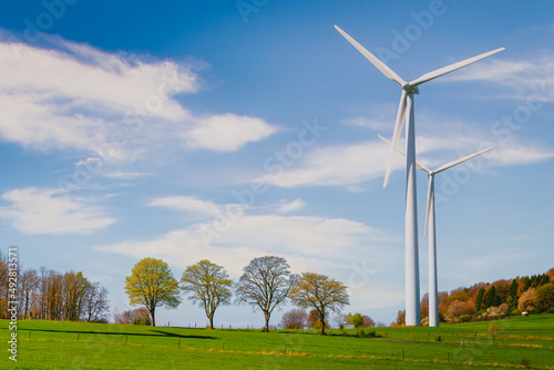 windkraftanlagen neben kleinen  bäumen auf dem feld unter dem blauen himmel photo