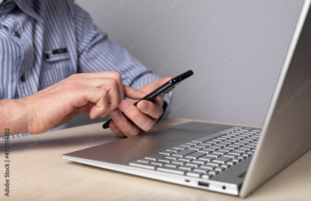 Man hands closeup holding phone while sitting at table with laptop. Using gadgets for work, education, social communication. High quality photo Man hands closeup holding phone while sitting at table with laptop. Using gadgets for work, education, social communication. High quality photo