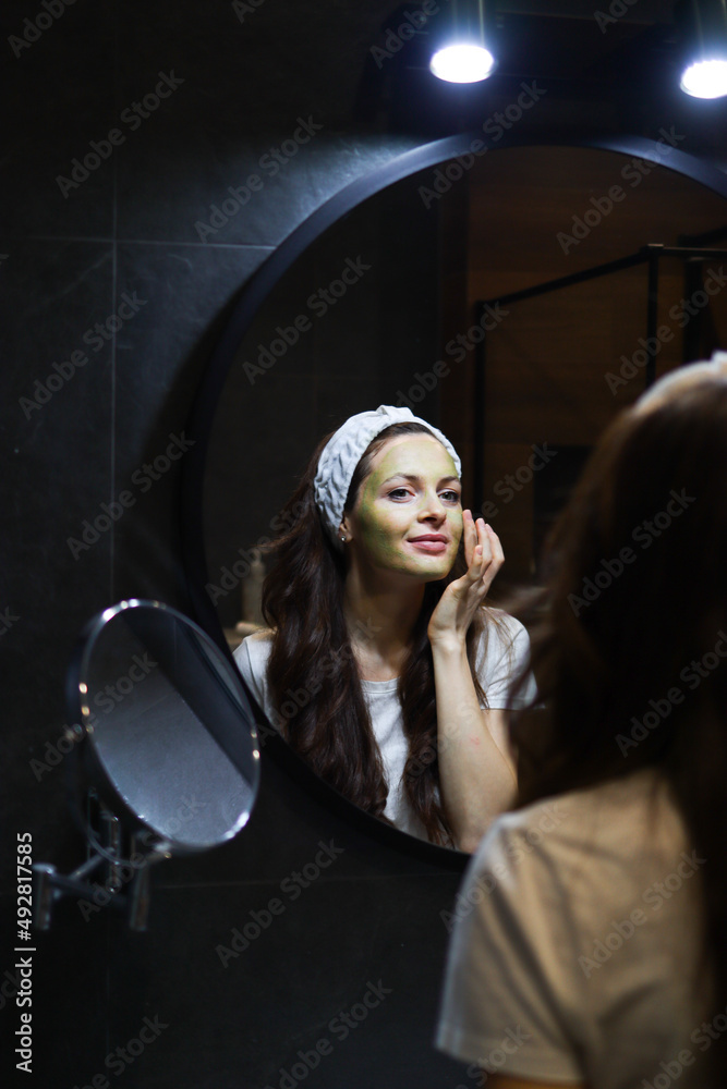 Girl taking care of oily complexion by using green clay mask. Woman in headband