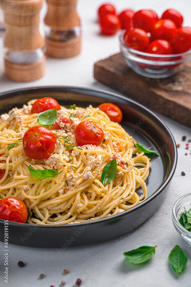 Pasta with baked feta with cherry tomatoes and herbs on a gray background.