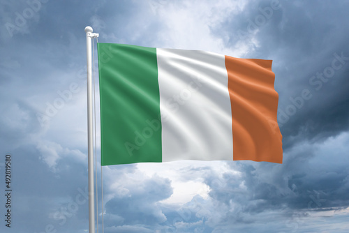 Irish flag on a flagpole waving in the wind on a cloudy sky background. Flag of Ireland