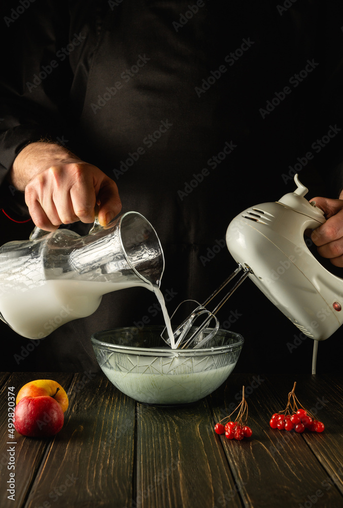 Preparing milkshake and fruit with an electric hand mixer. Refreshing drink  by the hands of the chef in the kitchen Stock Photo